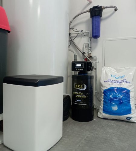 Installation complète d’un adoucisseur d’eau E.C.L. avec bac à sel, filtre violet et sac de sel en pastilles dans une buanderie.